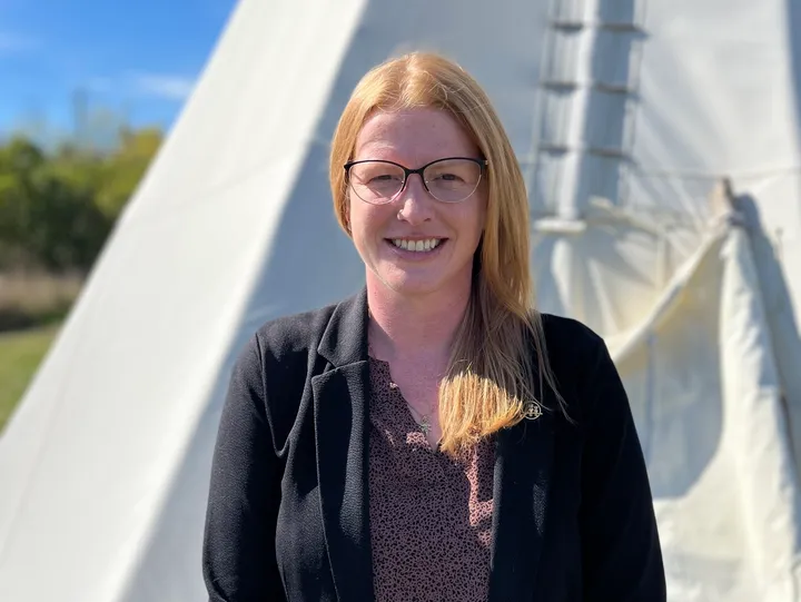 Smiling person standing near a white tent.