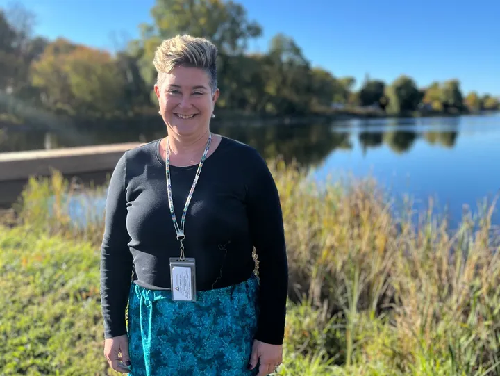 Smiling person standing by a serene lake.