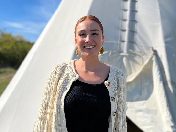 Smiling woman standing in front of tipi.