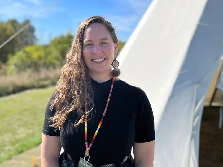 Smiling person outdoors near large tent.