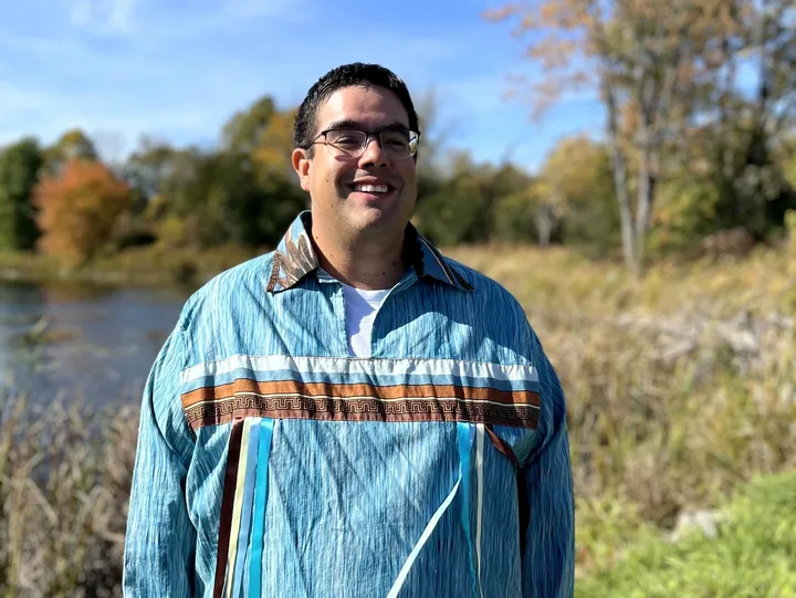 Smiling man outdoors in traditional attire.