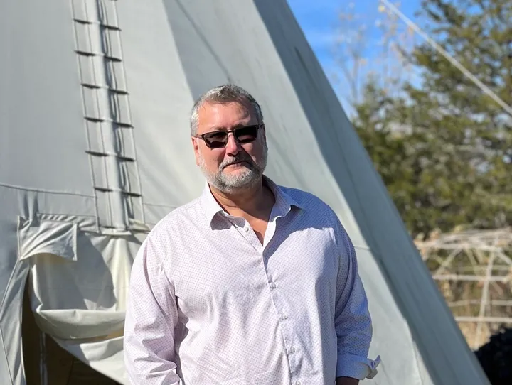 Man standing in front of a tipi.