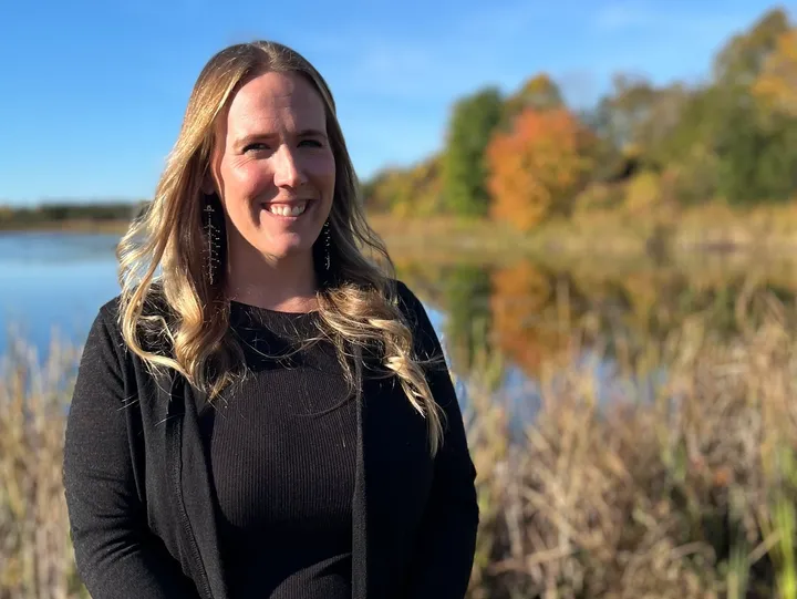 Smiling woman by lake with autumn trees.