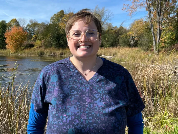 Smiling person standing near a scenic lake.