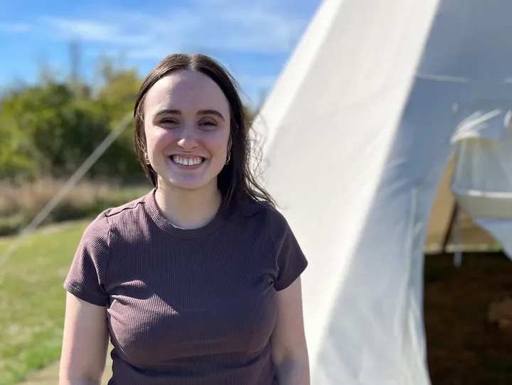 Smiling person standing beside a tent.