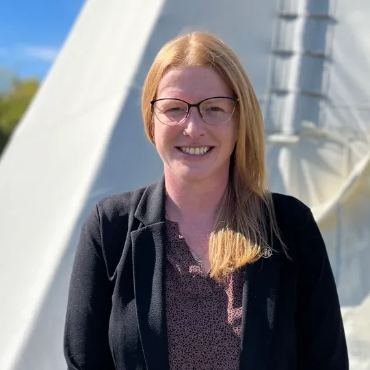 Smiling person standing near a white tent.