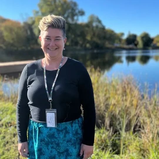 Smiling person standing by a serene lake.