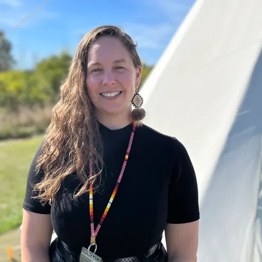Smiling person outdoors near large tent.