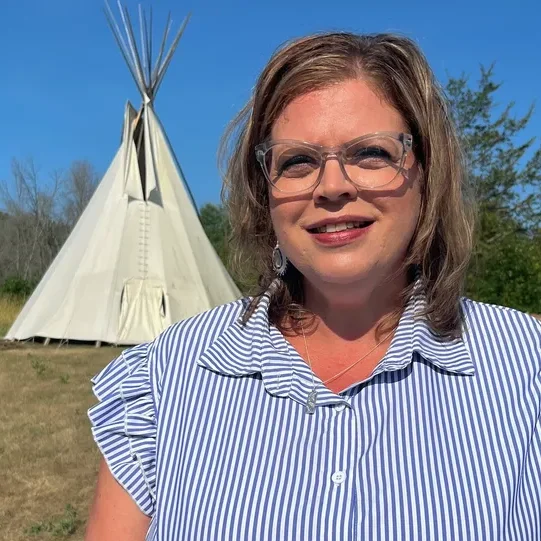 Woman smiling near a tipi outdoors.