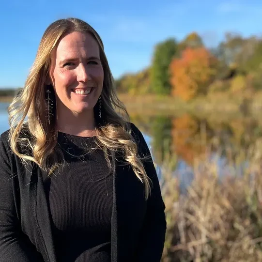 Smiling woman by lake with autumn trees.