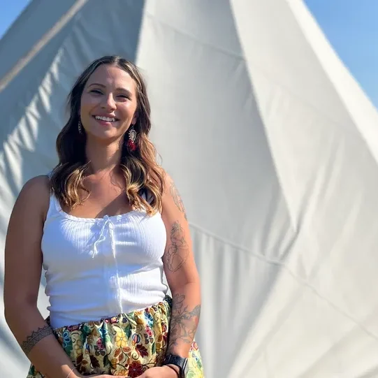 Smiling woman standing in front of teepee.